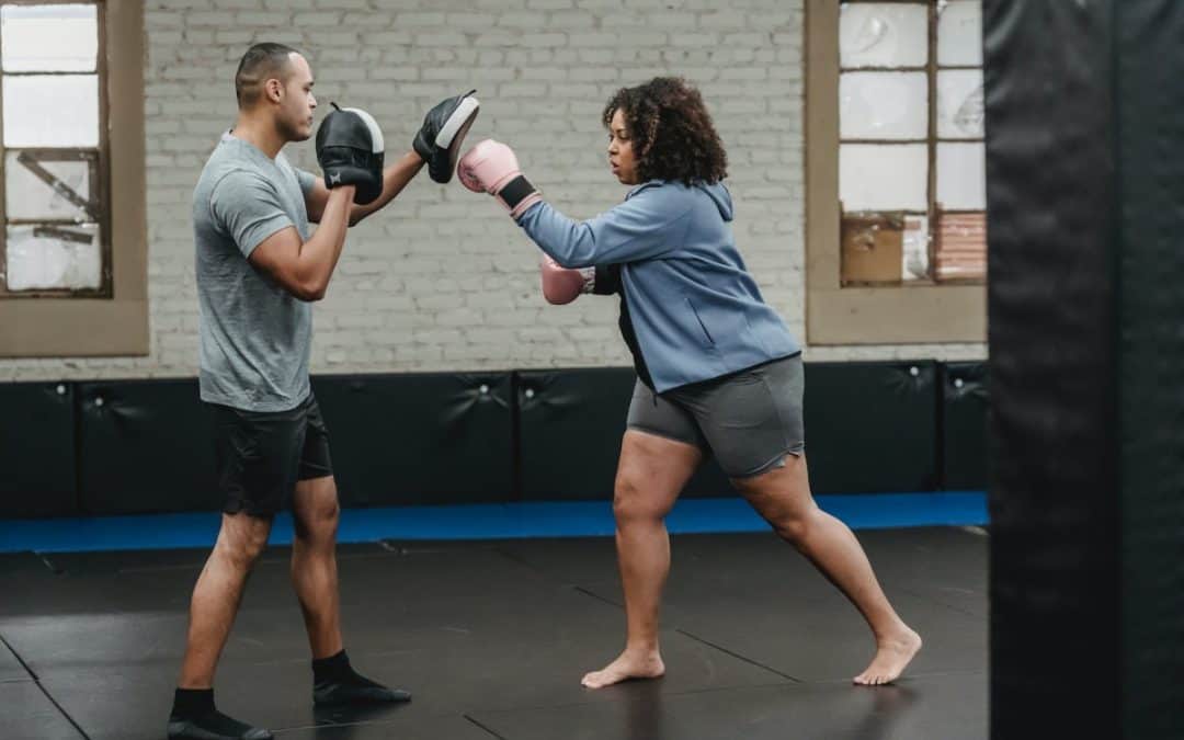 focused black plump female punching boxing paw of ethnic trainer