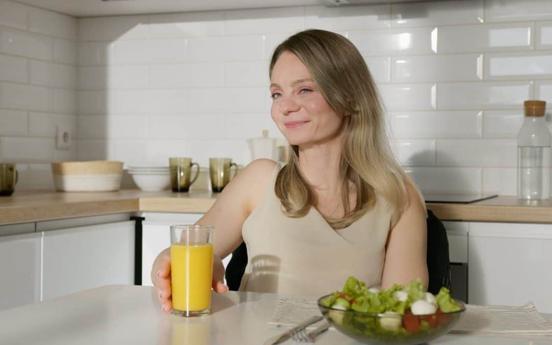 woman sitting by the table with an orange juice and vegetable salad